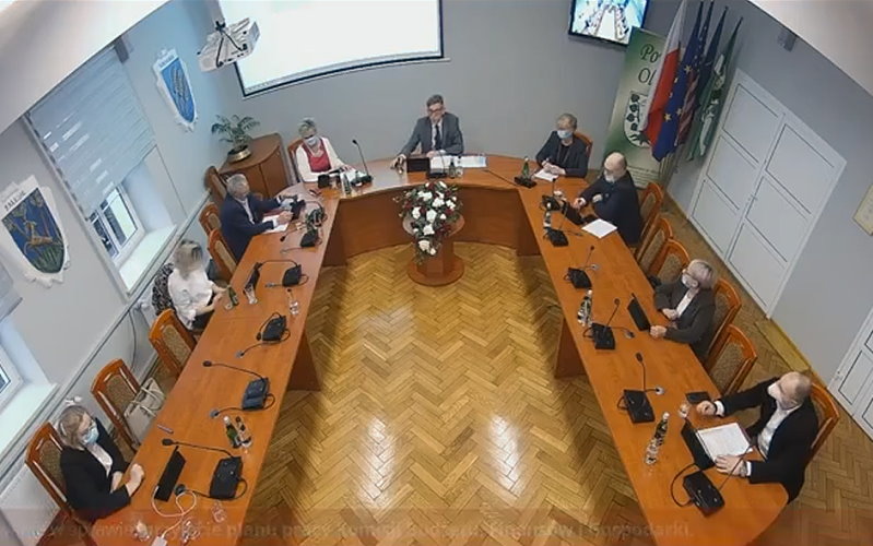 Sala Starostwa Powiatowego w Olecku w czasie sesji. Radni siedzą przy stole w sali urzędu.