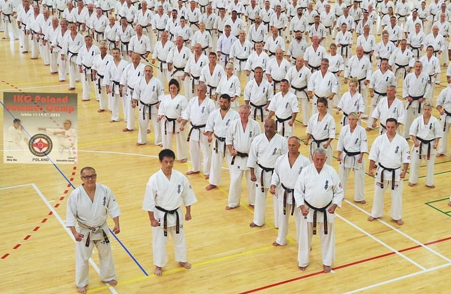 Kilkadziesiąt osób stoi w sali. Są oni ustawieni w rzędach. Są to zawodnicy karate i są ubrani w kimono.