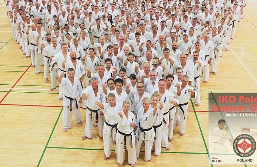 Kilkadziesiąt osób stoi obok siebie w sali. Są to zawodnicy karate i są ubrani w kimono.